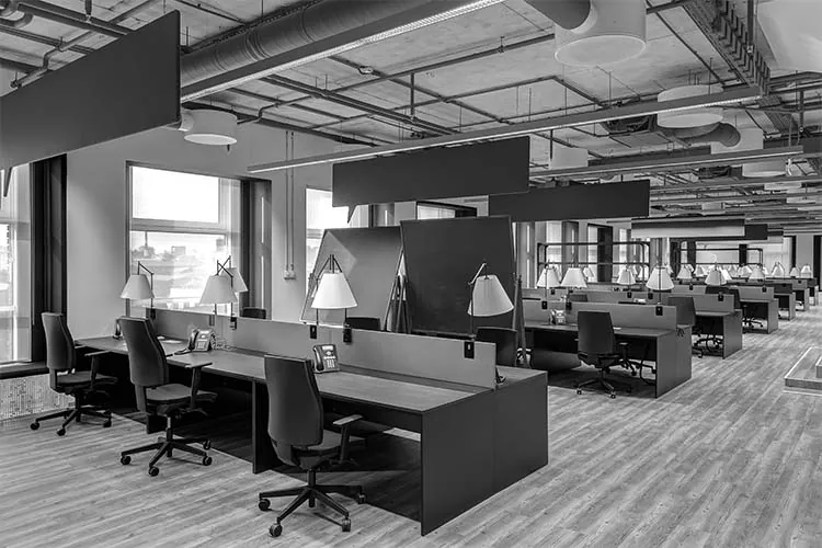 Open-plan office with rows of desks under an exposed industrial ceiling